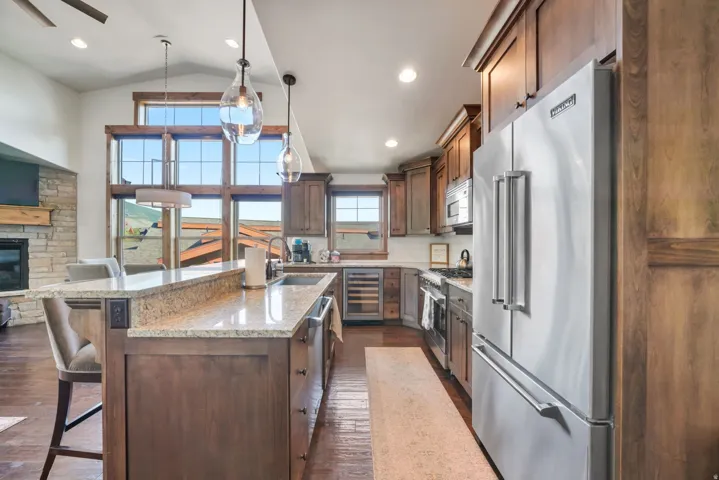 Open-concept kitchen featuring wood cabinetry, stainless steel appliances, a stone island with seating, and a vaulted ceiling with extensive window fenestration