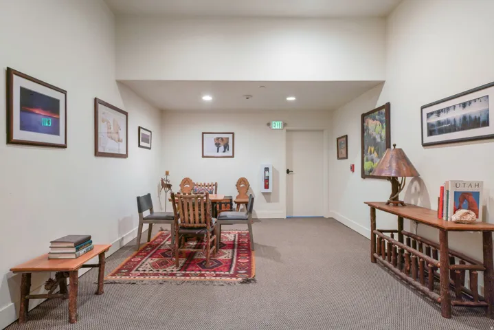 Carpeted hallway featuring recessed lighting and a white door with an illuminated exit sign