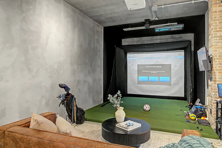 Dedicated indoor recreation space featuring a projection screen, turf flooring, and a projector