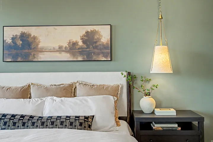 Upholstered headboard with an adjacent dark-tone nightstand and a brass-finish pendant light fixture