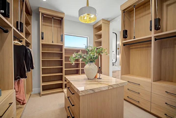 Custom built-in closet system featuring natural wood-finish cabinetry, a central island with a stone countertop, integrated shelving, and multiple hanging rods with retractable mechanisms