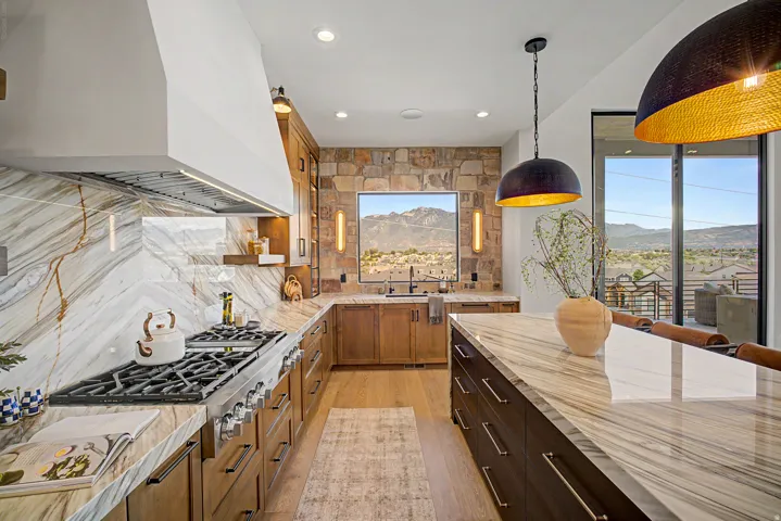 Gourmet kitchen featuring a professional-grade range, full-height stone slab backsplash, custom wood cabinetry, a large center island with seating, and expansive sliding glass doors