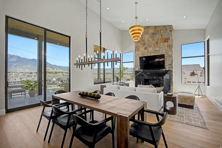 Open-concept living space with light wood-finish flooring, a stone-clad fireplace, and expansive windows