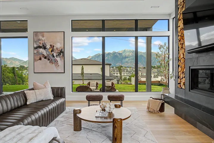 Living area featuring expansive floor-to-ceiling windows, light wood-finish flooring, and a contemporary fireplace with a dark stone surround