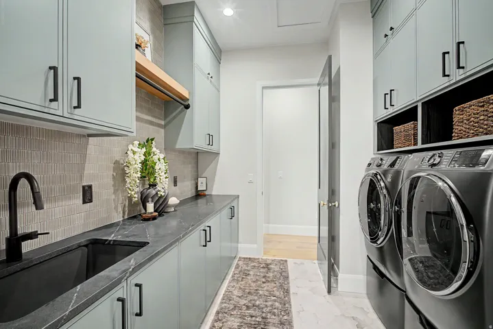 Dedicated laundry room featuring light blue cabinetry with matte black hardware, a black stone countertop, and a black sink with a matte black faucet