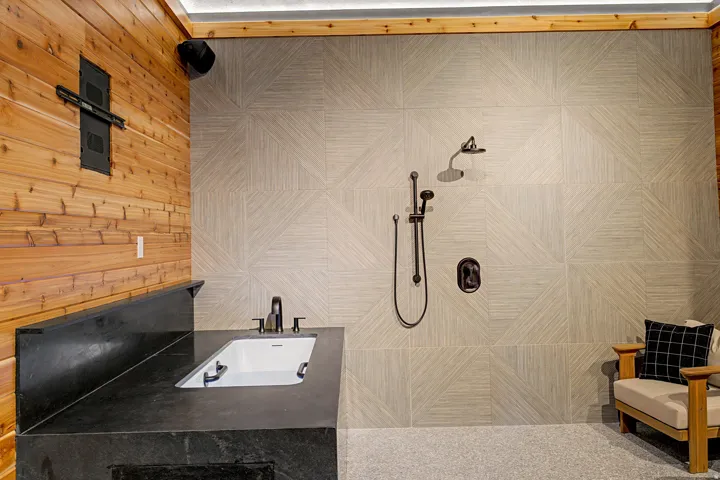 Spacious shower area featuring a large format geometric tiled wall, a built-in black stone countertop with an undermount sink, and wood plank wall paneling