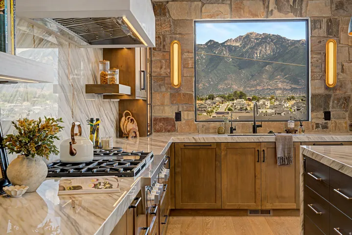 Gourmet kitchen featuring a large picture window with a mountain backdrop, a built-in range, a stainless steel range hood, stone wall accents, and light wood-finish flooring