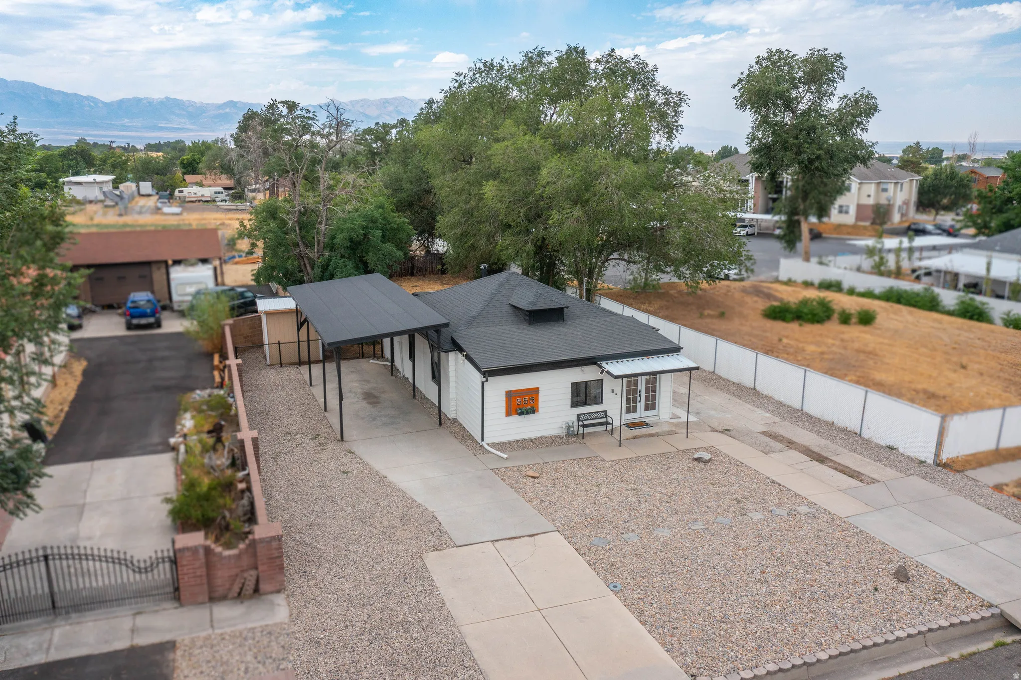 White exterior with a dark shingle roof, featuring an attached carport with a dark metal roof