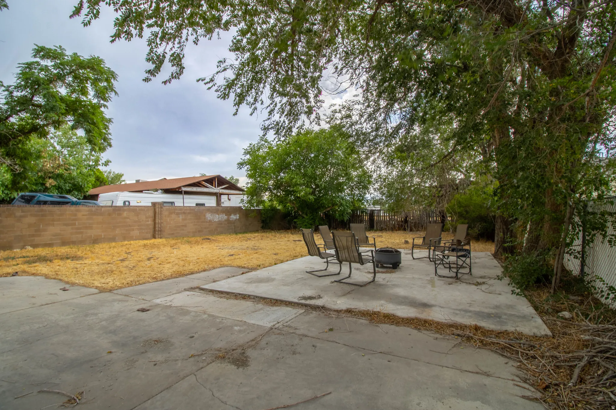 Expansive backyard featuring a concrete patio, mature trees, and a block wall perimeter