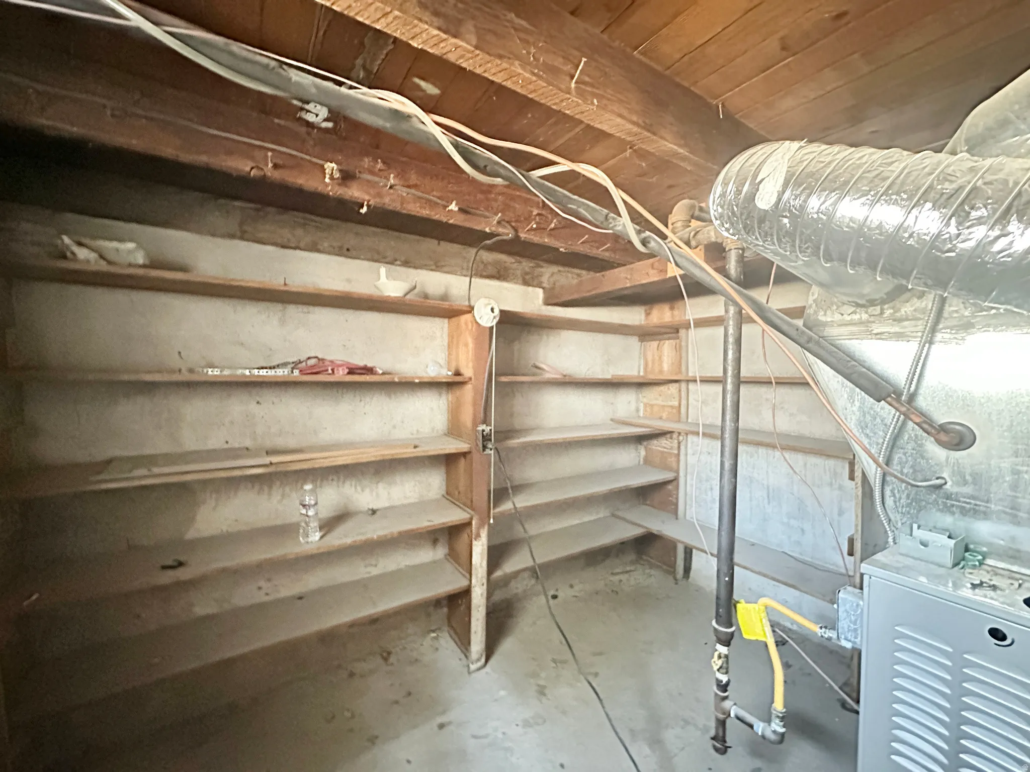 Storage area featuring built-in wood shelving, exposed ceiling joists, and concrete flooring