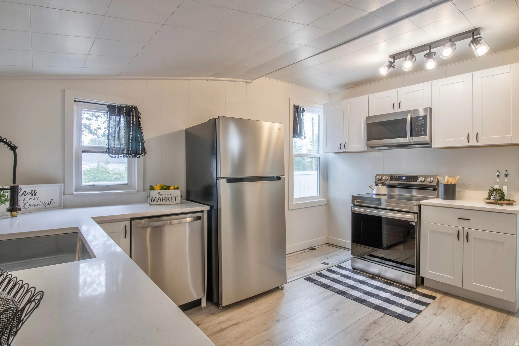 Kitchen featuring white cabinetry with dark hardware, quartz countertops, and stainless steel appliances including a refrigerator, dishwasher, and electric range with an over-the-range microwave