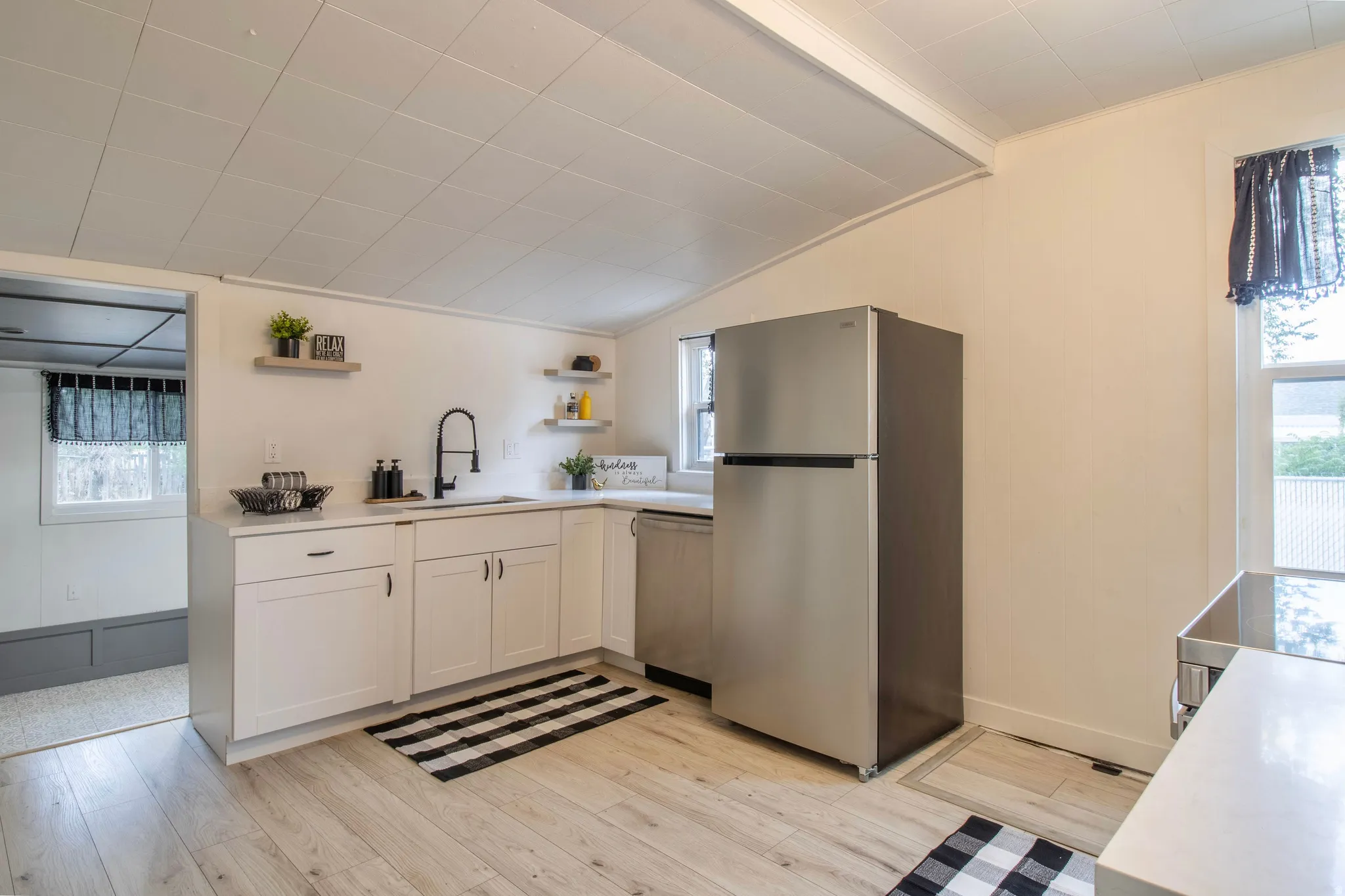 Kitchen featuring light wood-finish flooring, white cabinetry with black hardware, a stainless steel refrigerator, a stainless steel dishwasher, and a white sink with a matte black faucet