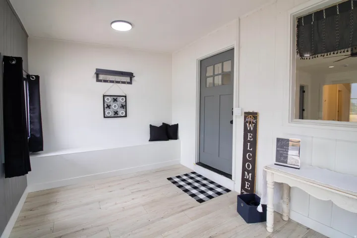 Foyer featuring wood-finish flooring, a built-in bench, a gray paneled door with glass inserts, and white vertical paneling