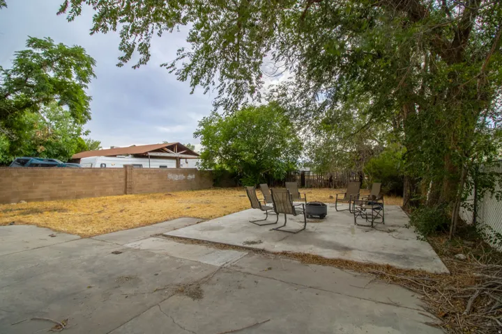 Expansive backyard featuring a concrete patio, mature trees, and a block wall perimeter