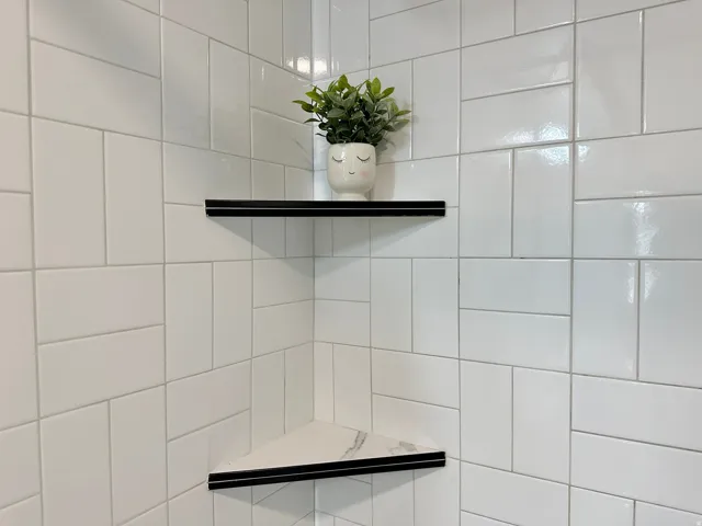 White rectangular wall tiles with a varying pattern, complemented by two built-in corner shelves