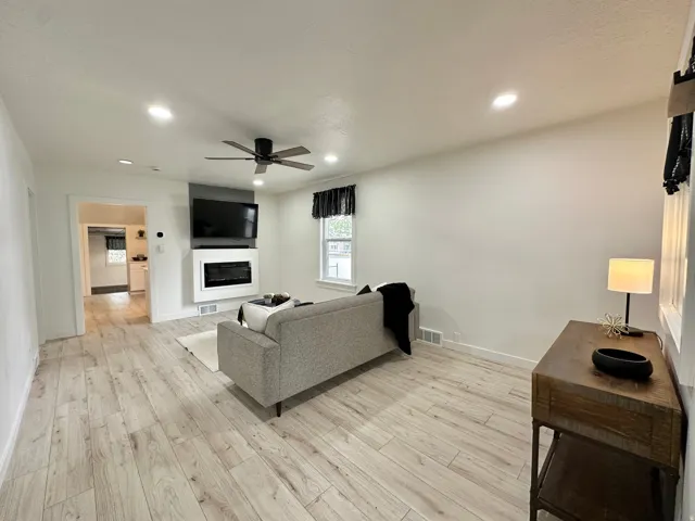 Living area featuring light wood-finish flooring, fireplace, recessed lighting, and a contemporary ceiling fan