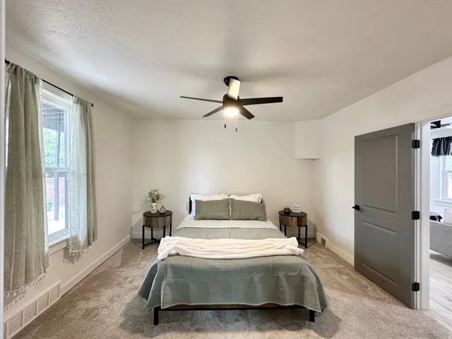 Spacious room featuring neutral carpeting, a ceiling fan with integrated lighting, and a modern paneled door