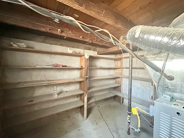 Storage area featuring built-in wood shelving, exposed ceiling joists, and concrete flooring
