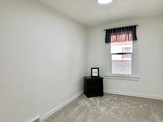 Bright room featuring a window with white trim, light-colored carpet flooring, white walls, and a ceiling-mounted light fixture