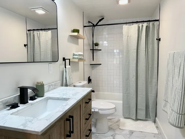 Bathroom featuring a wood-finish vanity with a single basin sink and quartz-finish countertop, black fixtures, a wall-mounted mirror, a tiled shower-tub combination and a bidet toilet.