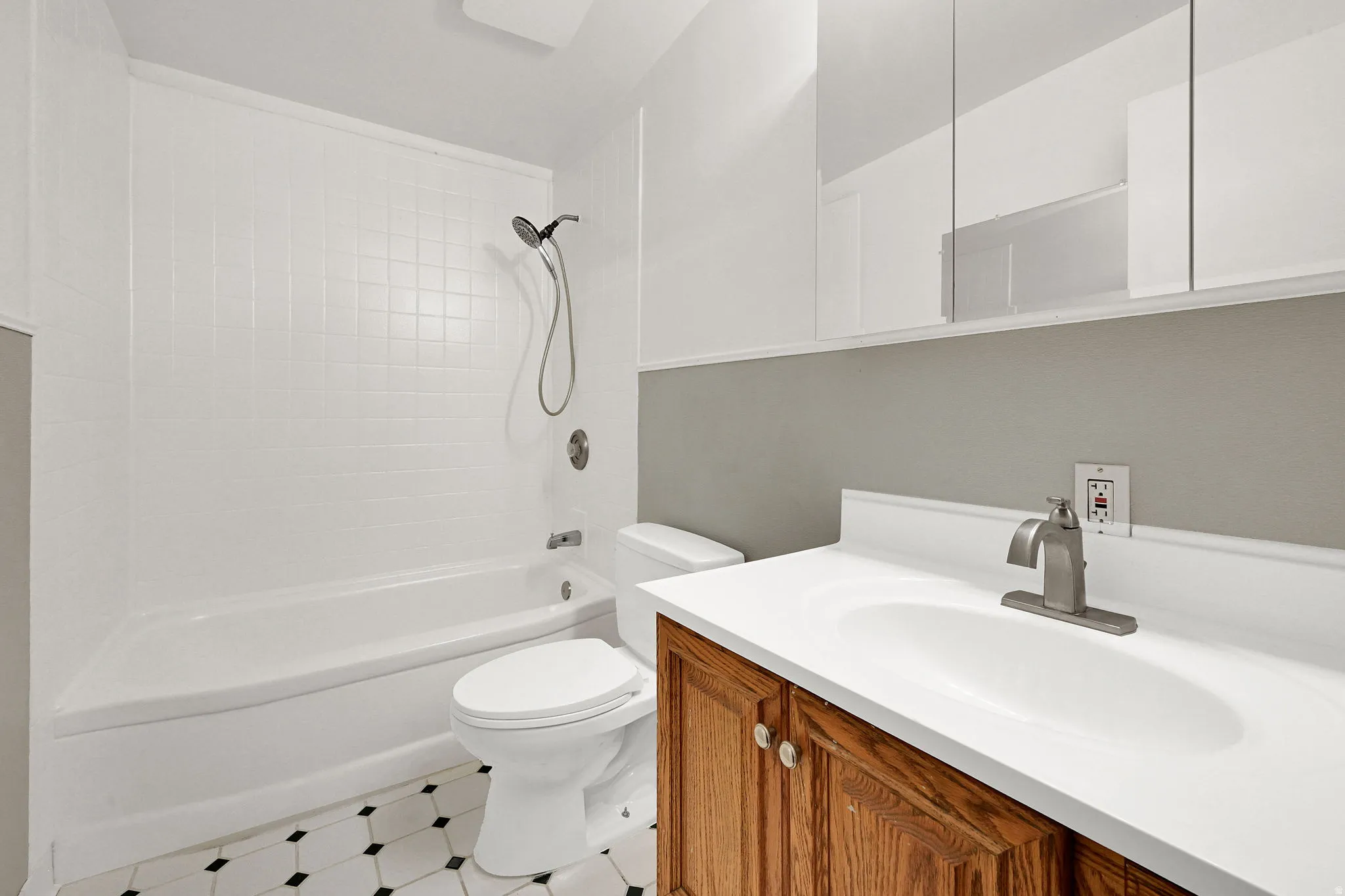Bathroom featuring a tiled tub and shower combination, white toilet, single vanity with wood-finish cabinetry, white countertop, and hexagonal floor tiling