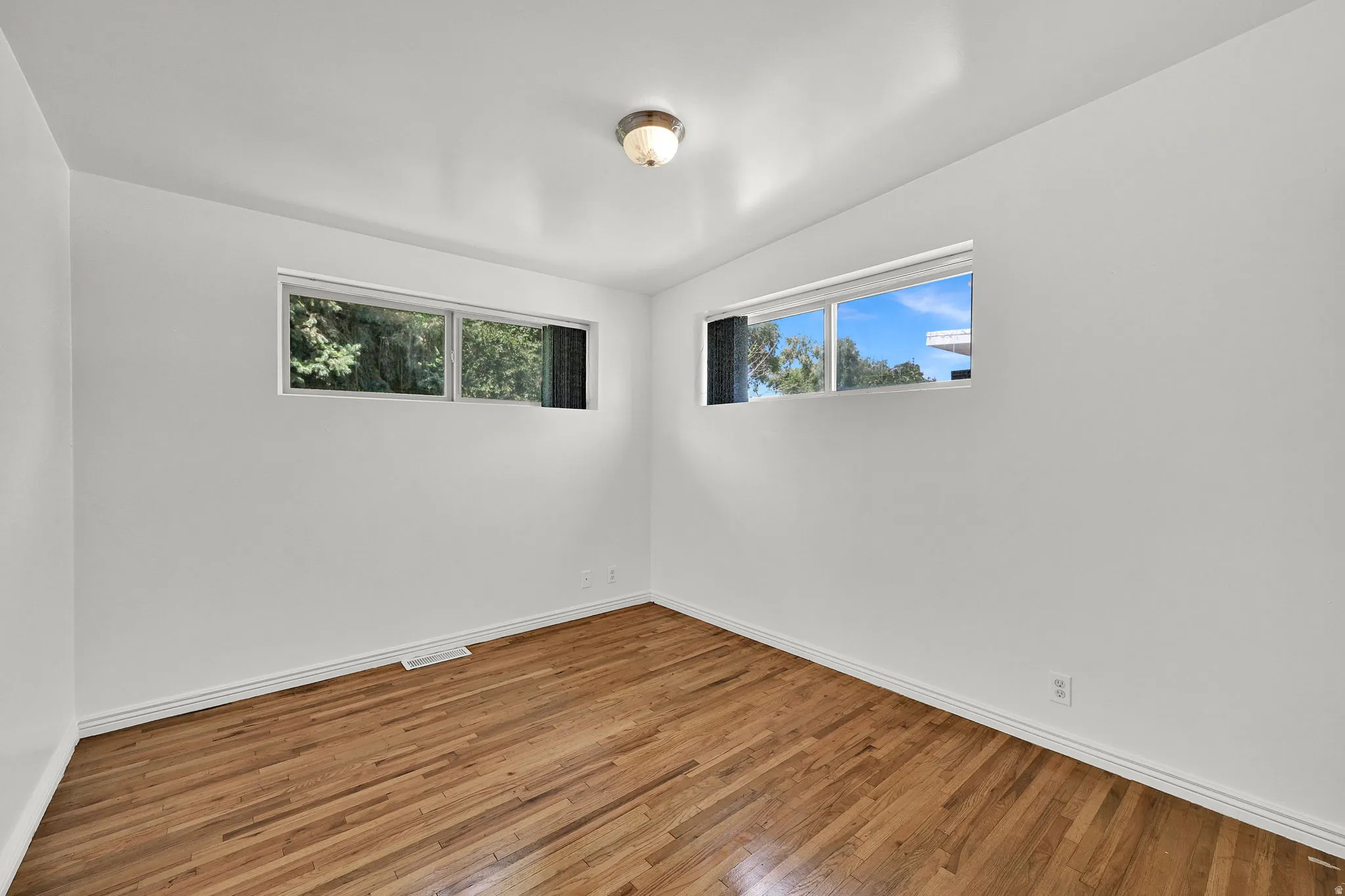 Spacious room featuring wood-finish flooring, white walls, and a ceiling-mounted light fixture