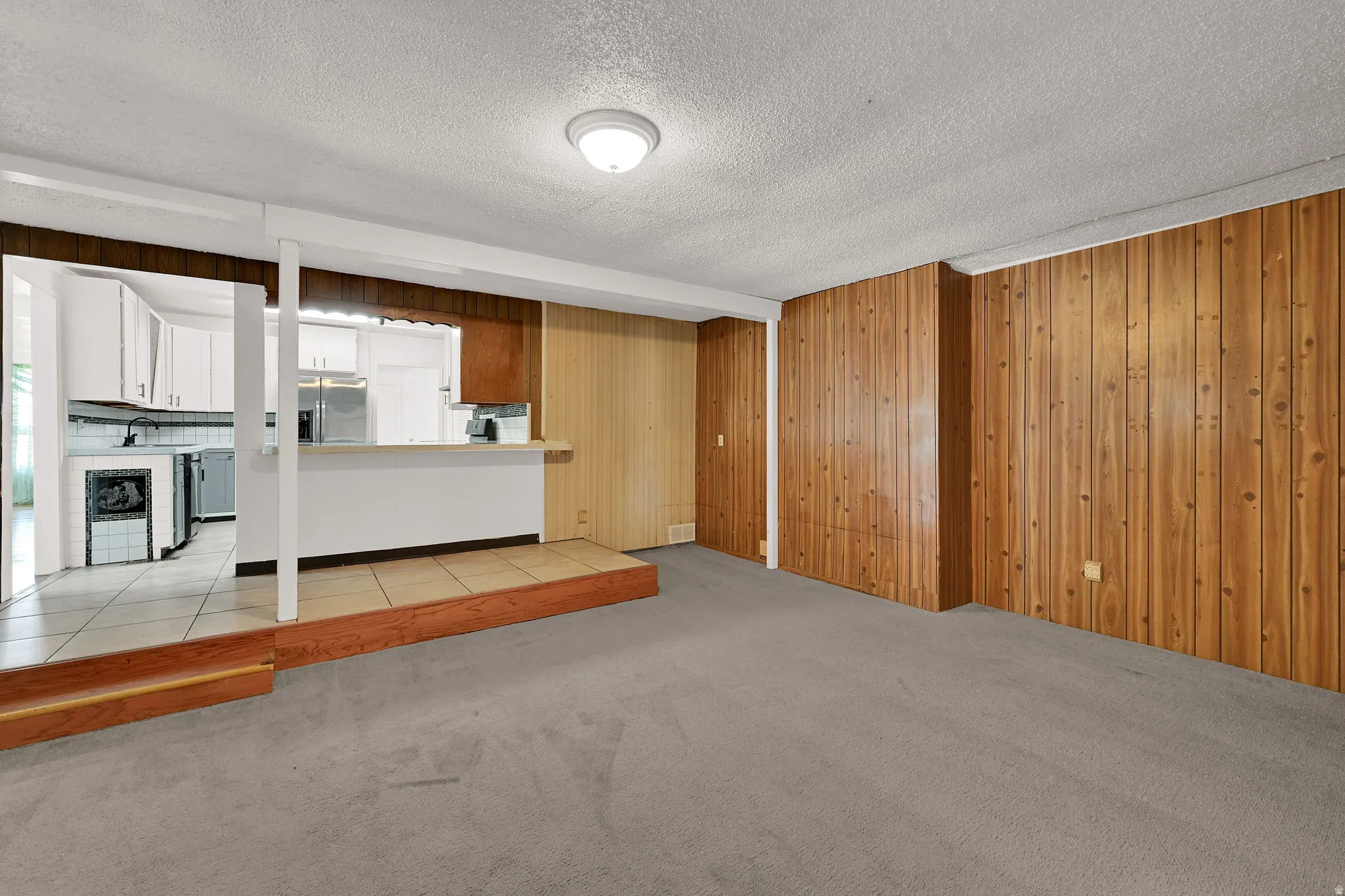 Spacious living area featuring light wood paneling, gray carpeting, and a built-in breakfast bar
