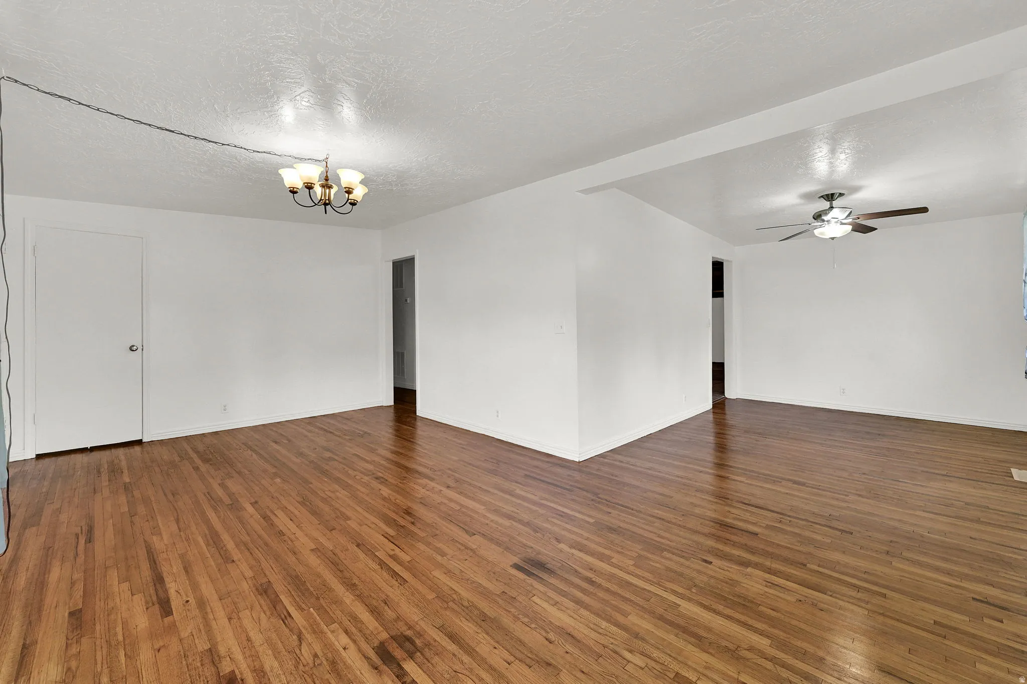 Spacious living area featuring polished wood flooring, a ceiling-mounted light fixture, and a ceiling fan