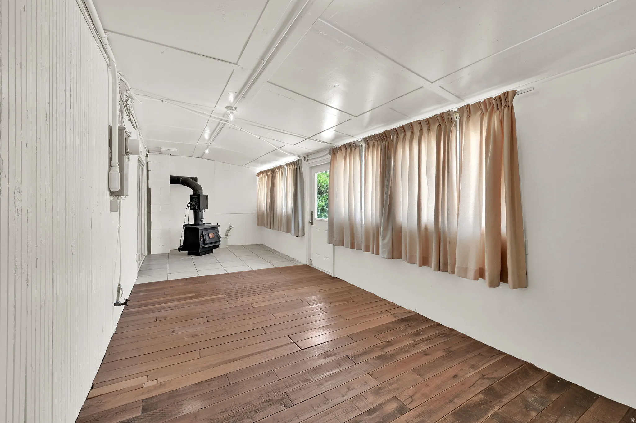 Interior space featuring wood-finish flooring, white paneled walls, and a black wood-burning stove on a tiled hearth