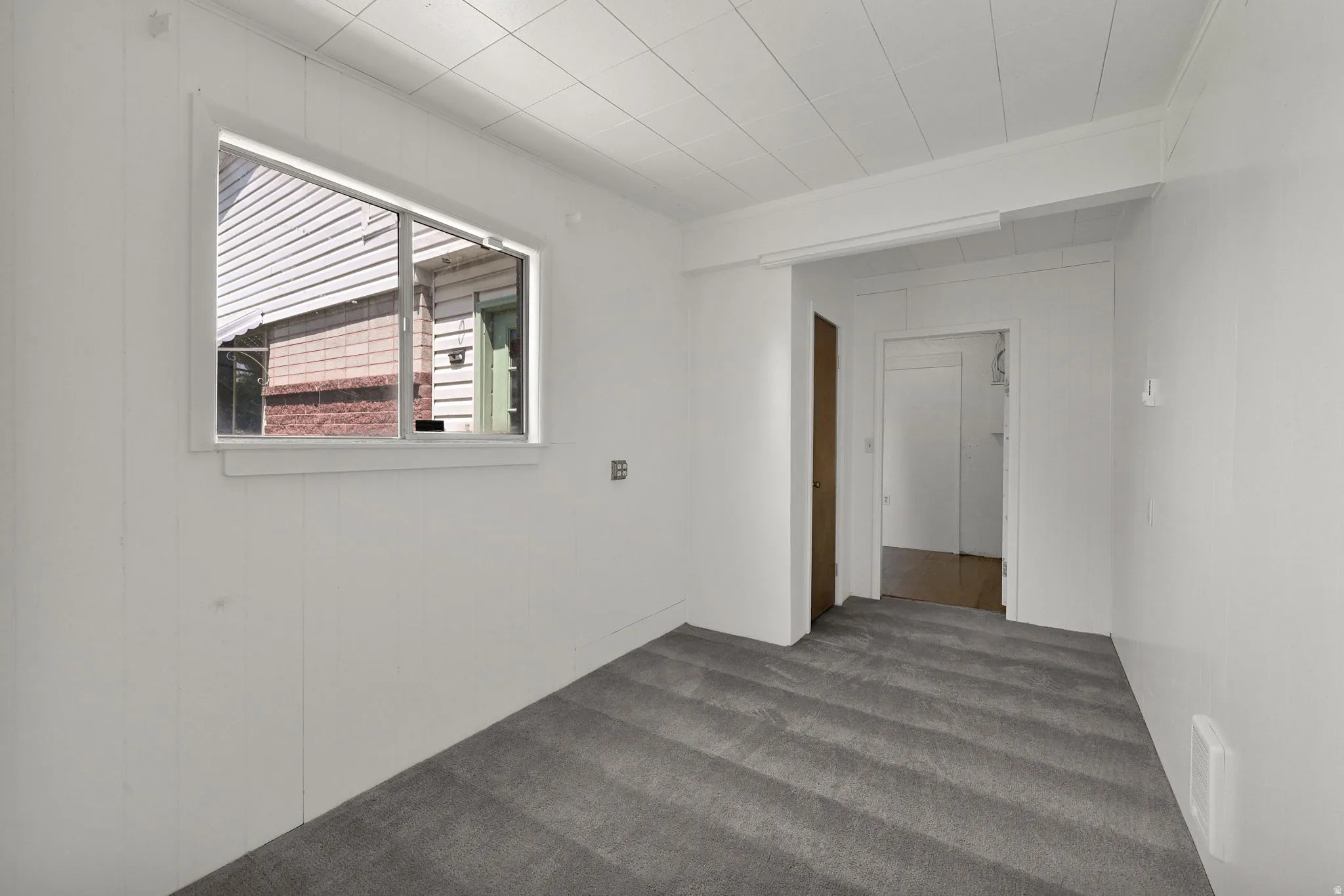Room featuring a single-pane window, horizontal paneling walls, a white paneled ceiling, and gray patterned carpet