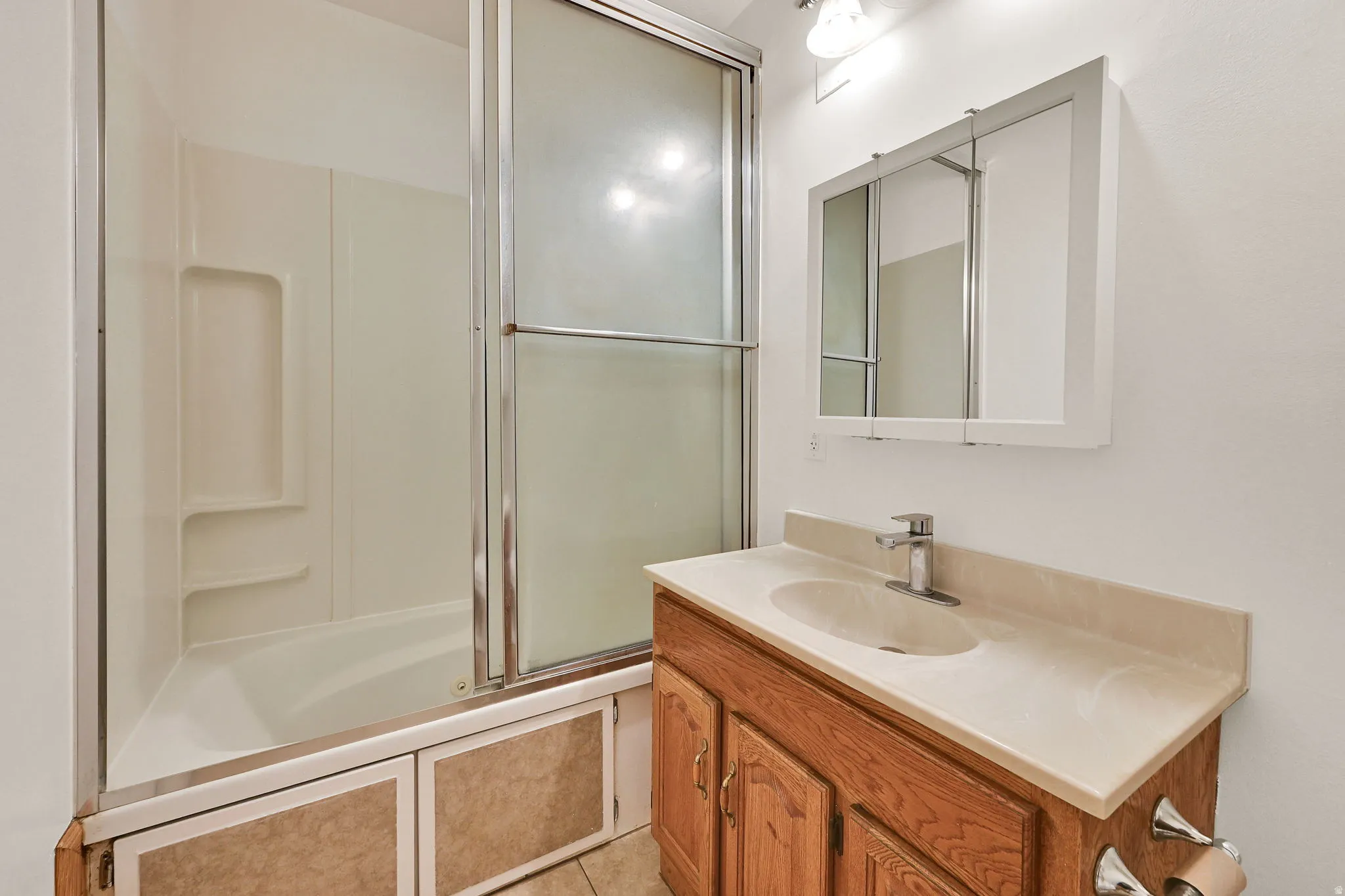 Bathroom featuring a white bathtub with sliding glass doors, a vanity with wood-finish cabinetry, a light-toned countertop, and an integrated sink
