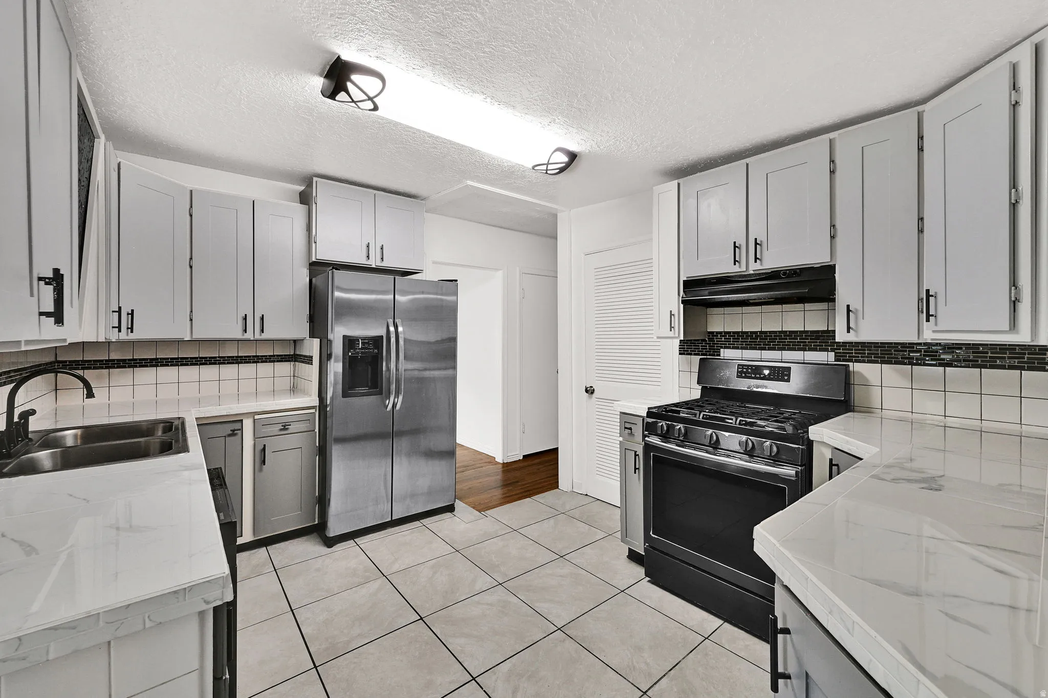 Kitchen featuring light gray cabinetry, white countertops, tile flooring, stainless steel appliances, and a tile backsplash