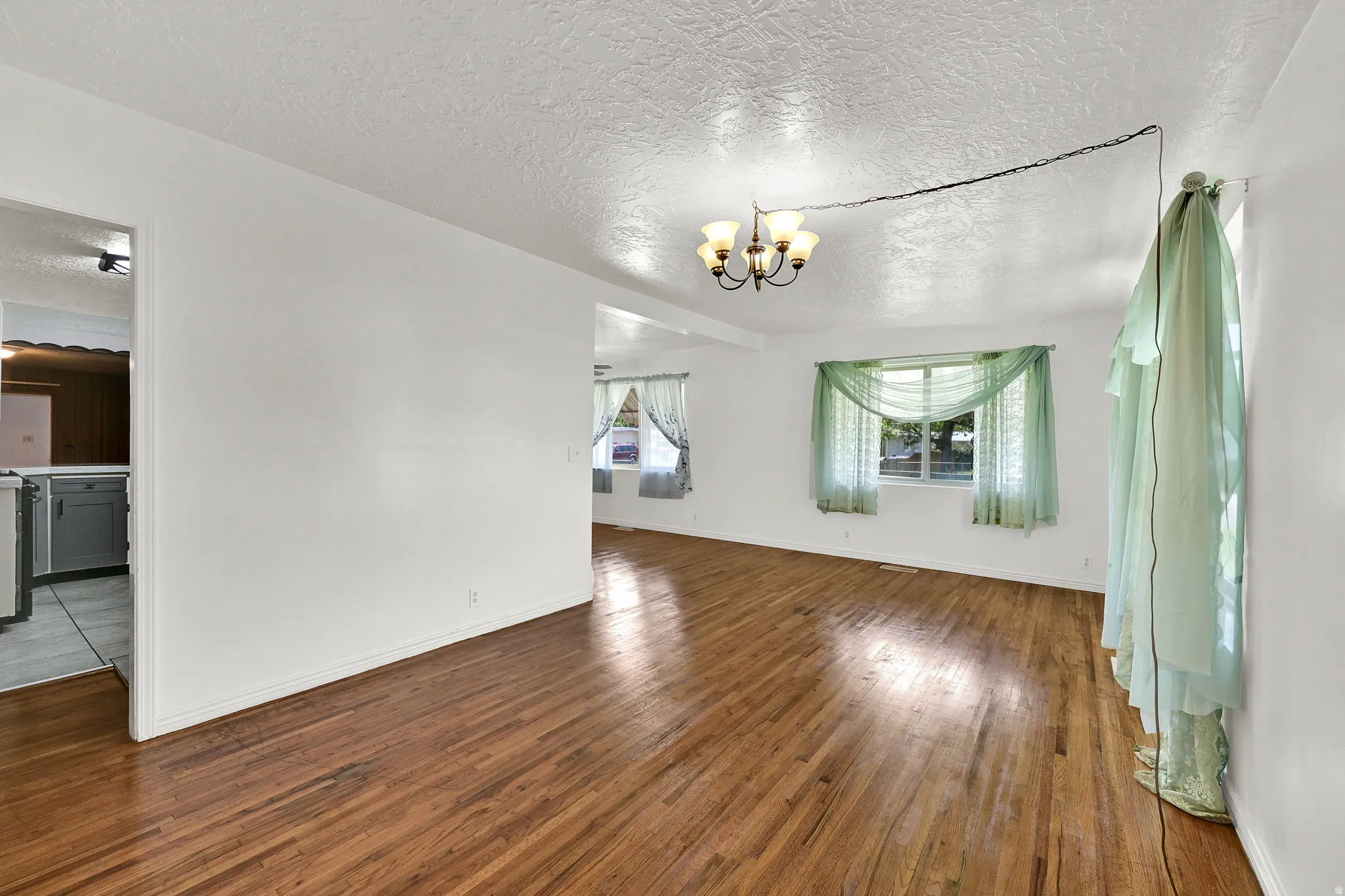 Expansive room featuring rich wood flooring, white walls, and a multi-bulb ceiling fixture