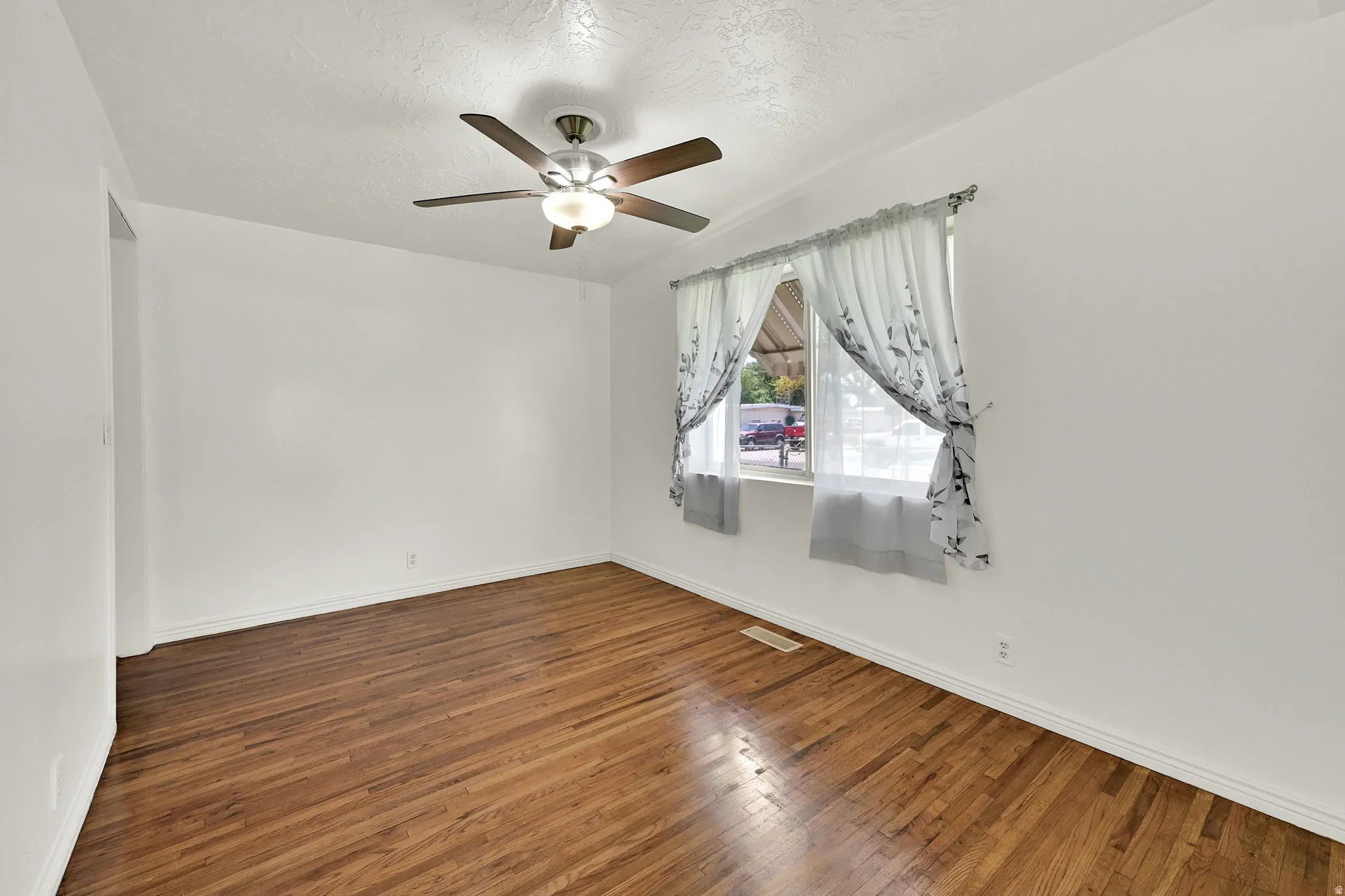 Bright interior space featuring wood-finish flooring, a contemporary ceiling fan with integrated lighting, and a window with natural light
