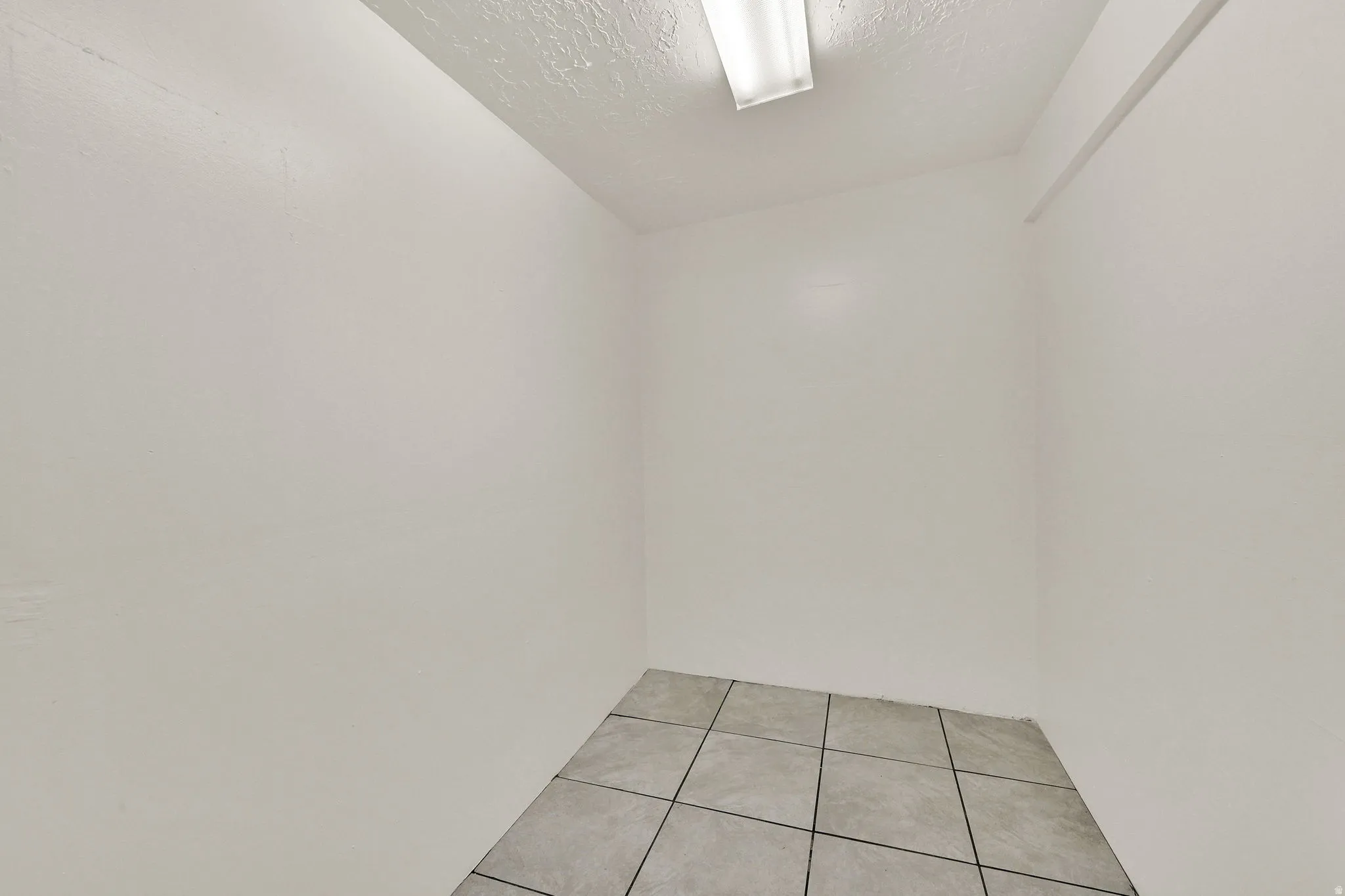 White-painted interior space featuring tile flooring and a ceiling-mounted fluorescent light fixture