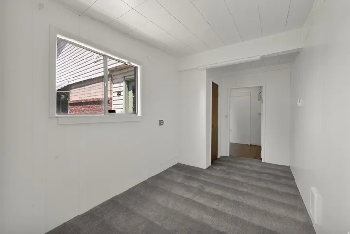 Room featuring a single-pane window, horizontal paneling walls, a white paneled ceiling, and gray patterned carpet