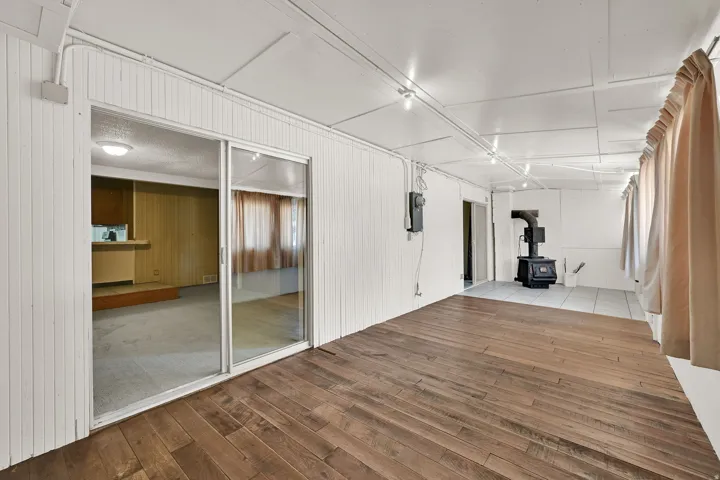 Spacious room featuring wood-finish flooring, white vertical plank walls, track lighting, and a freestanding black stove