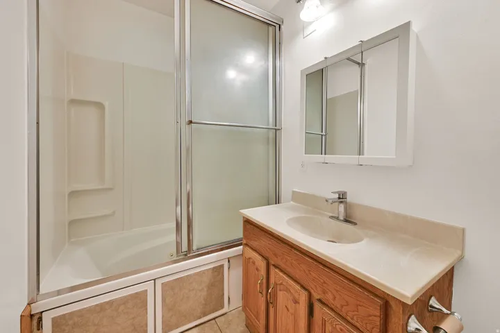 Bathroom featuring a white bathtub with sliding glass doors, a vanity with wood-finish cabinetry, a light-toned countertop, and an integrated sink