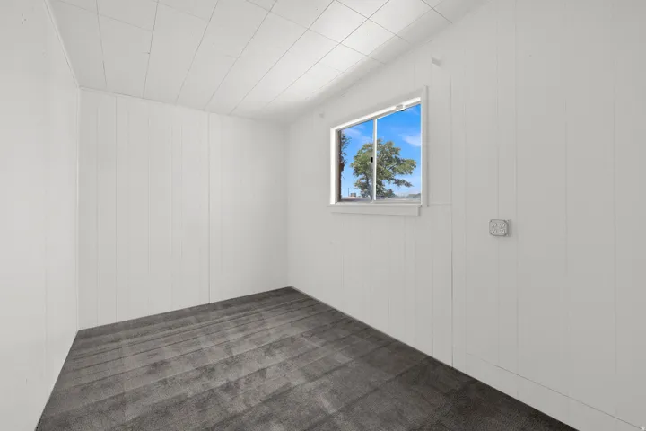 Room featuring white vertical paneling, gray patterned carpeting, a single window, and a white grid ceiling