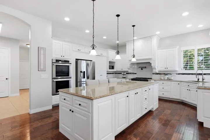 White cabinetry kitchen featuring a large central island with a granite countertop, stainless steel appliances, wood-finish flooring, and pendant lighting