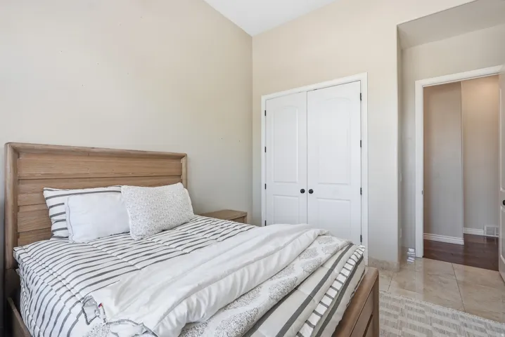 Vaulted ceiling room featuring a light wood-finish bed frame, dual white bifold closet doors, and light-toned tile flooring