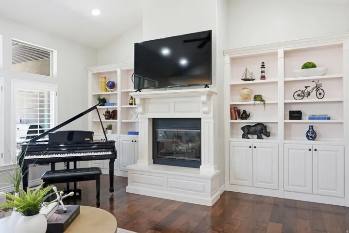 Living area featuring a fireplace with a detailed mantel, built-in shelving with lower cabinetry, and wood-finish flooring