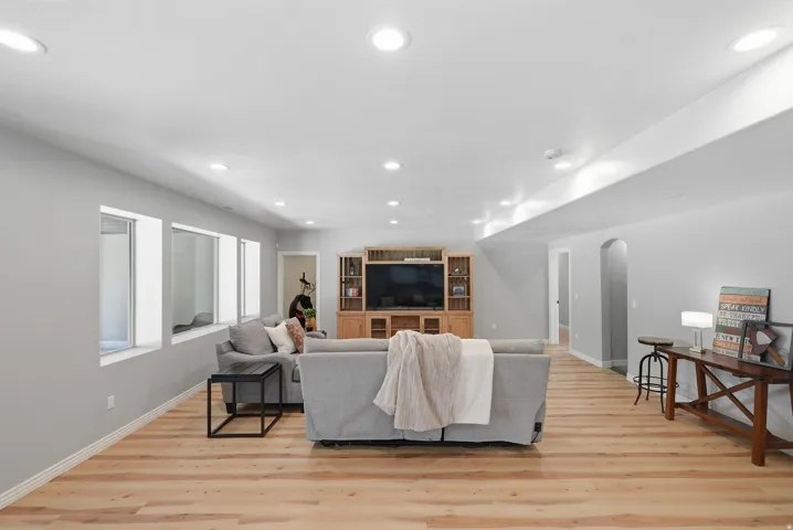 Spacious living area featuring light wood-finish flooring, recessed ceiling lights, and multiple windows