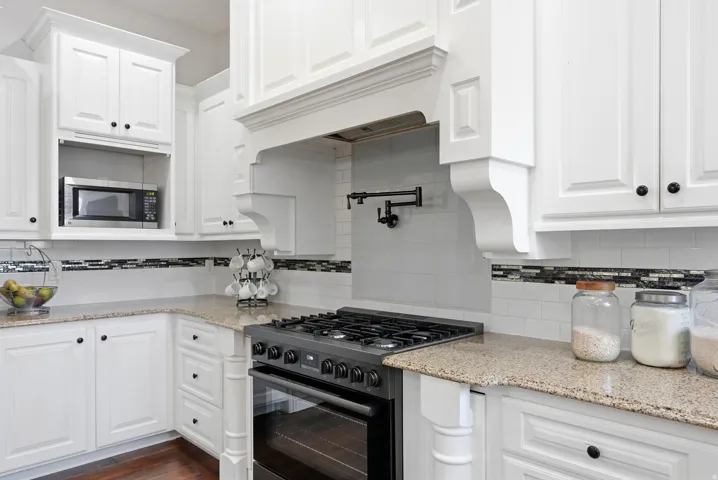White cabinetry with black hardware, stone countertops, and a subway tile backsplash featuring a decorative mosaic accent