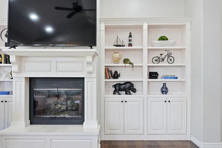 White-painted fireplace surround with mantel, flanked by built-in bookshelves featuring open shelving and lower cabinetry, all set against wood-finish flooring