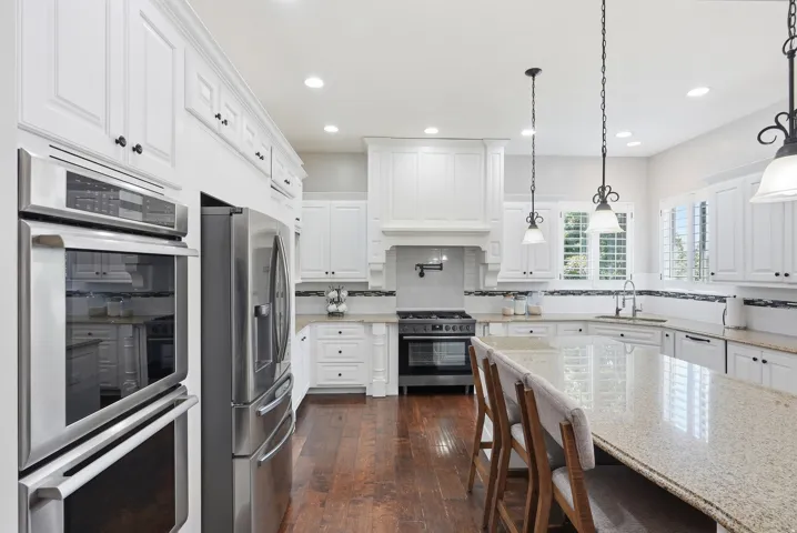 Gourmet kitchen featuring white cabinetry, stainless steel appliances, a large center island with a granite countertop, wood-finish flooring, and recessed lighting