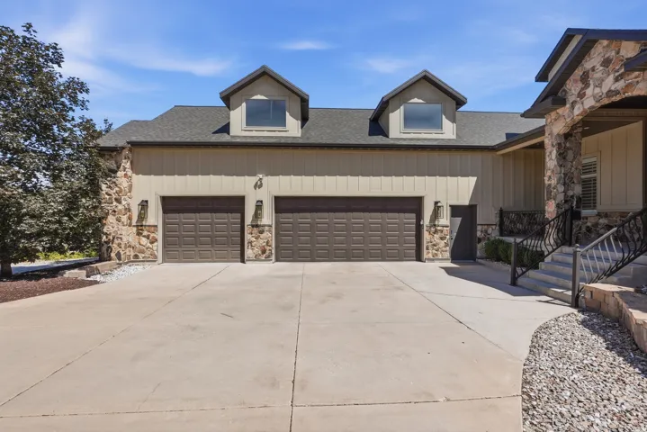 Exterior featuring two dormer windows, a two-car garage with individual doors, vertical board siding, and stone accents