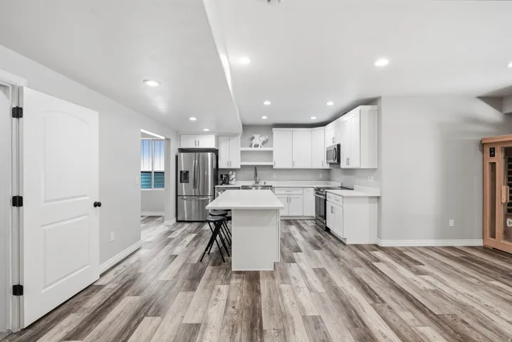Modern kitchen featuring white cabinetry, stainless steel appliances, a center island with seating, recessed lighting, and wood-finish flooring