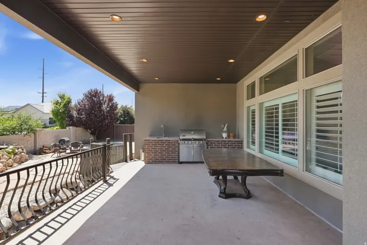 Covered patio featuring an outdoor kitchen with brick surround, recessed lighting, and a durable concrete surface