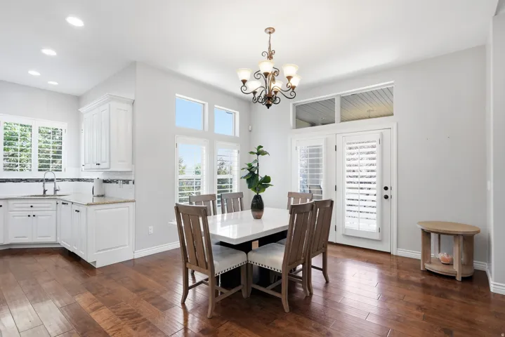 Open-concept dining area featuring wood-finish flooring, a decorative chandelier, and an abundance of natural light from multiple windows and French doors with plantation shutters